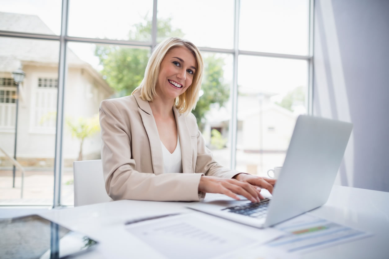 Glimlachende vrouw aan bureau achter een computer gebruikt iGuana iDM software om documenten te zoeken en te gebruiken die zij nodig heeft voor haar werk.